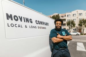 Man in Blue T-shirt and Black Pants Standing Beside White Van